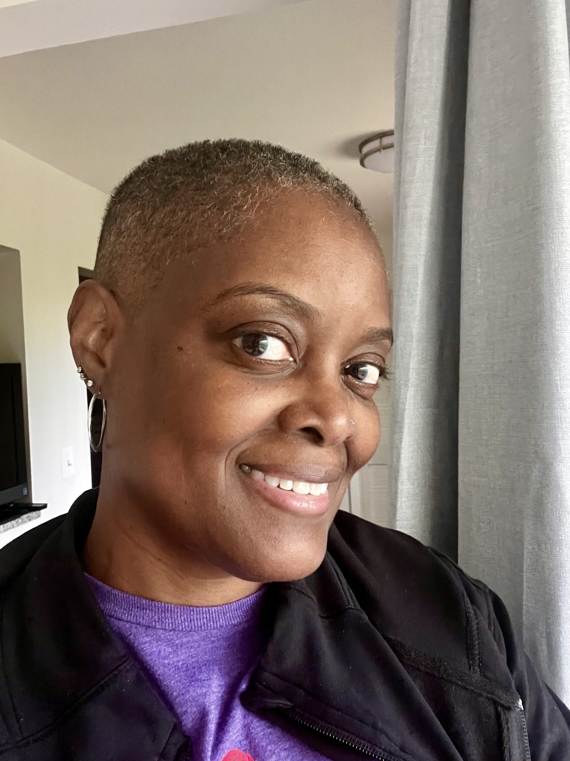 A woman confidently wearing a short haircut, revealing natural gray strands—a face seasoned by life, glowing with grace.

