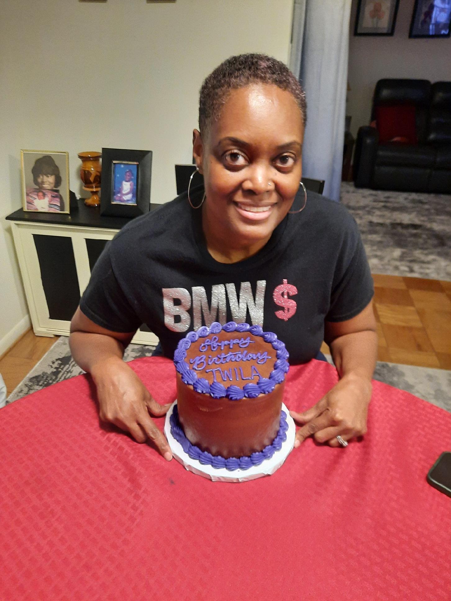 Tami Zanele smiling with her 54th birthday cake in front of her, a joyful moment captured during a simple at-home celebration.