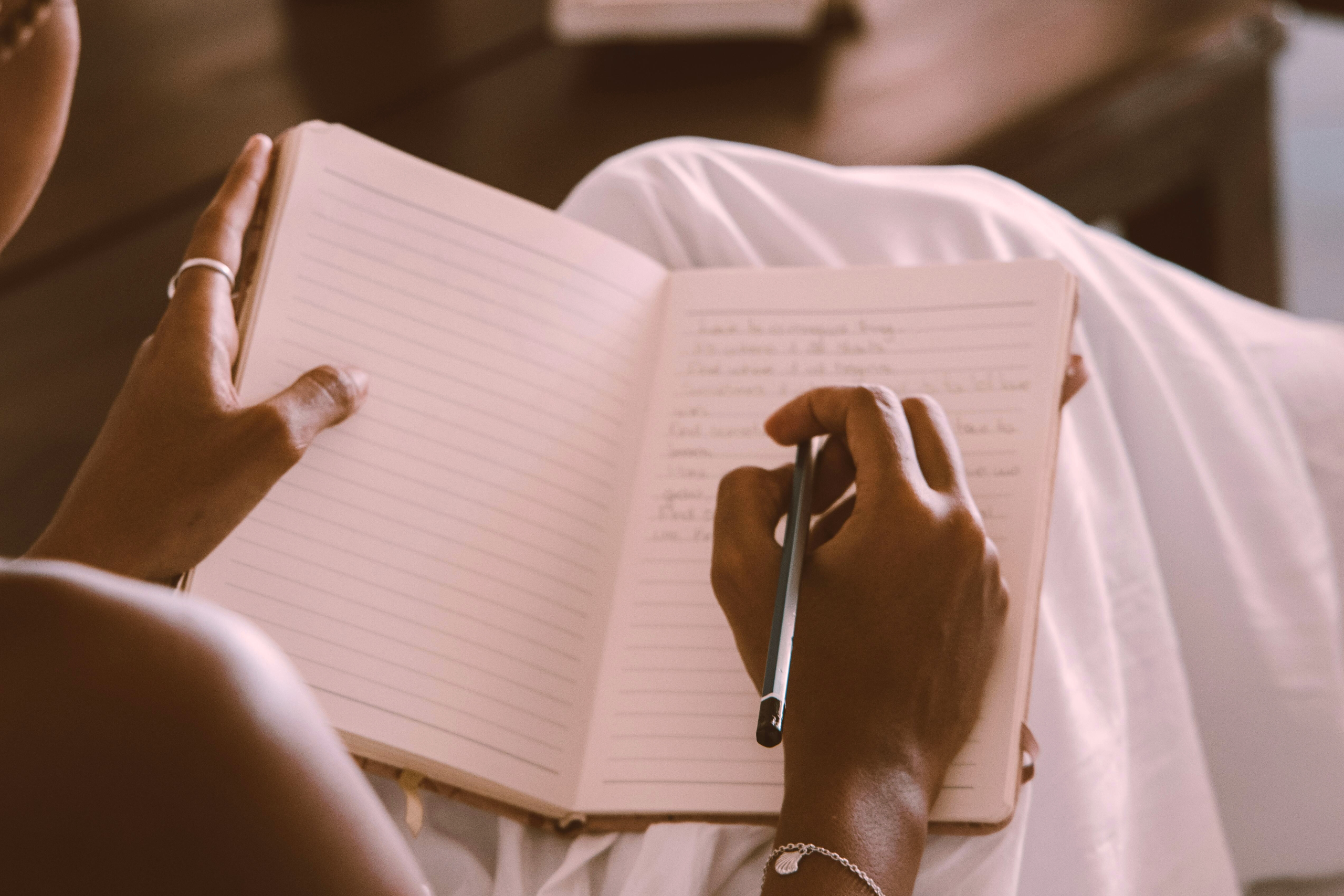Woman's hands holding a pen while writing in an open journal resting on her lap
