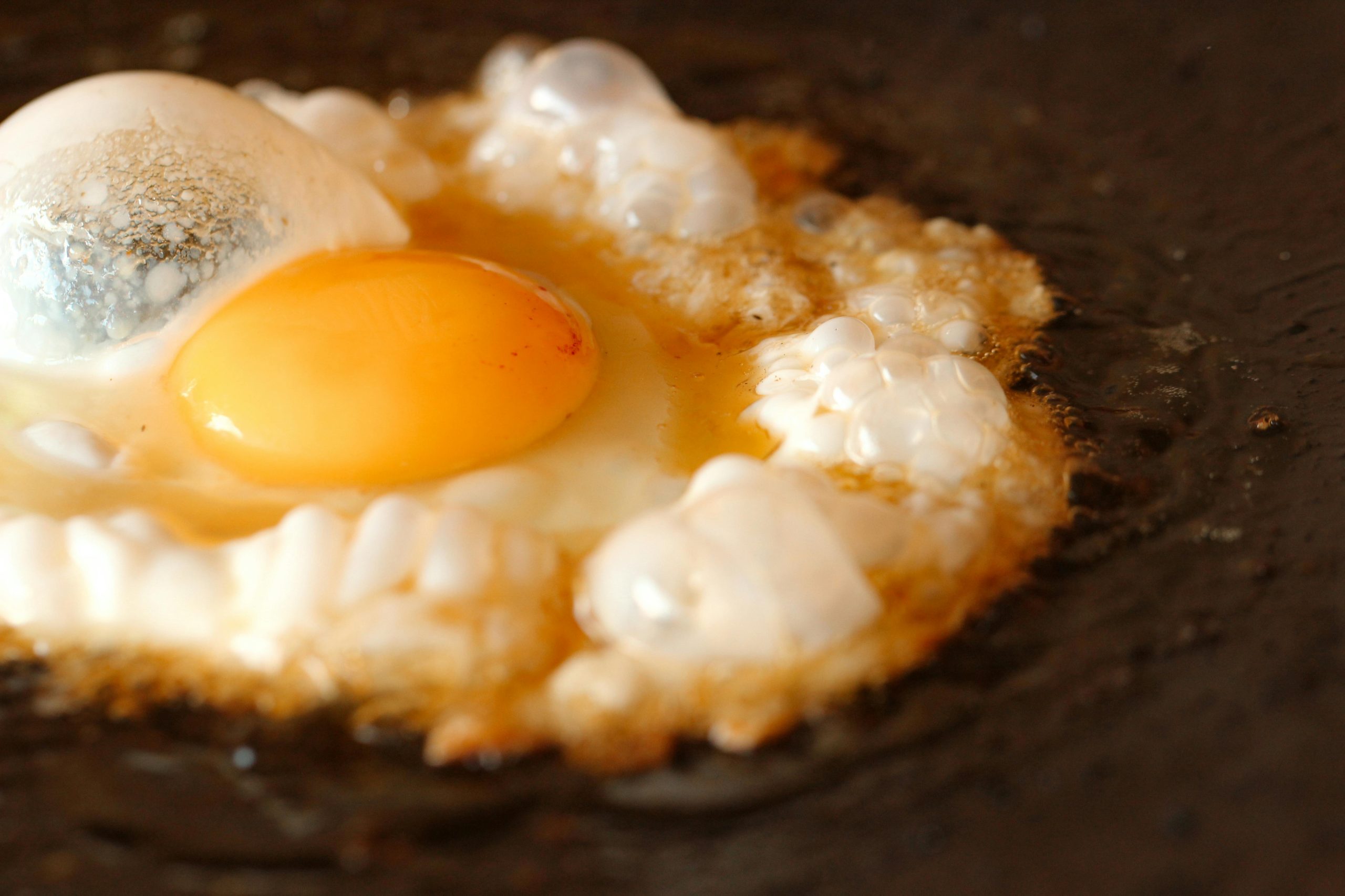 Egg frying and sizzling in a hot cast iron skillet.