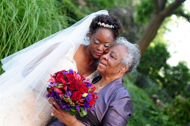 Tami Zanele as a bride leaning cheek to cheek with her grandmother Fannie on her wedding day, both holding a bouquet of red and purple flowers.